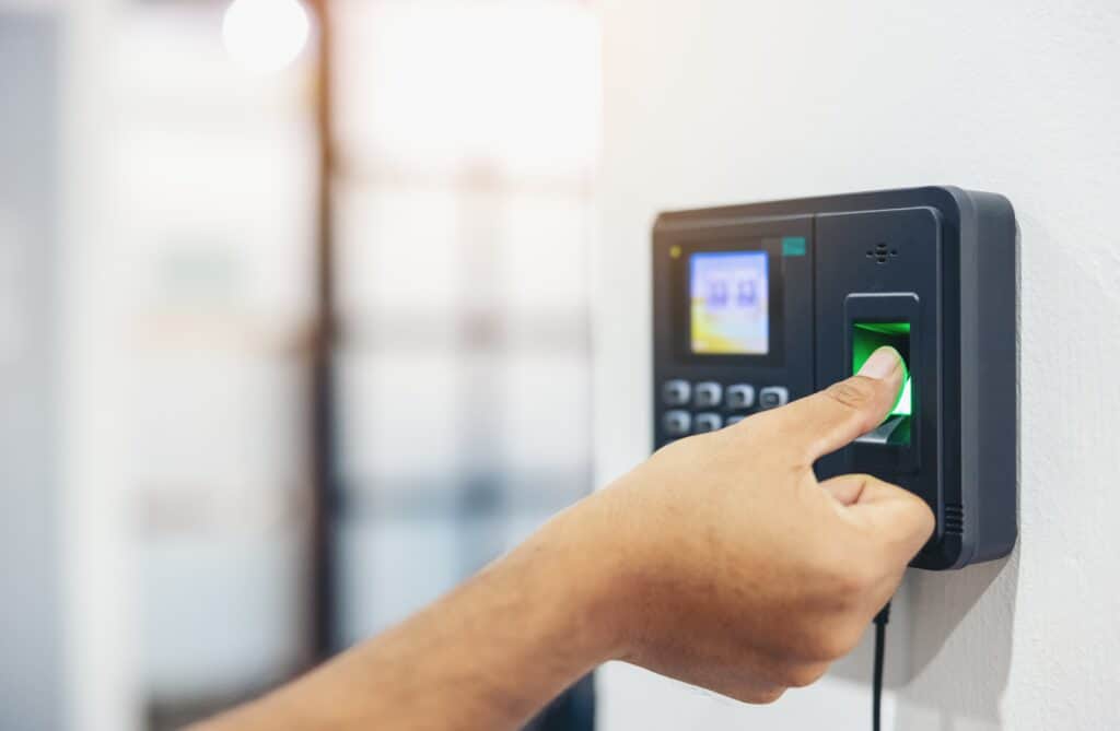 Employee using a fingerprint time attendance software device to clock in, demonstrating biometric time tracking technology mounted on a wall.